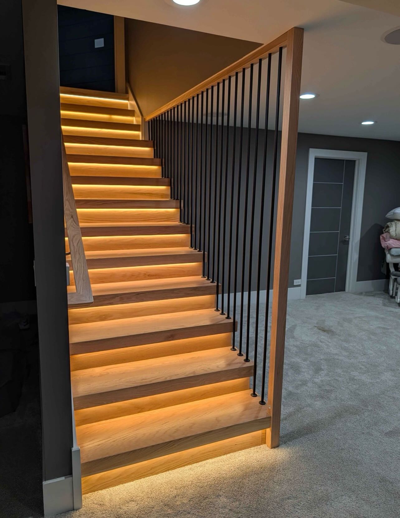 Custom staircase with LED under-tread lighting, oak treads and black metal balusters by LevelUp Renos London Ontario