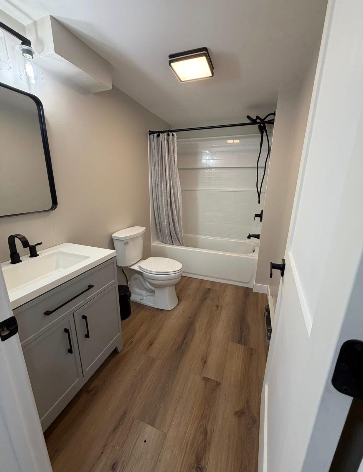 Basement bathroom with warm wood LVP floor, grey vanity and tub shower combination by LevelUp Renos London Ontario